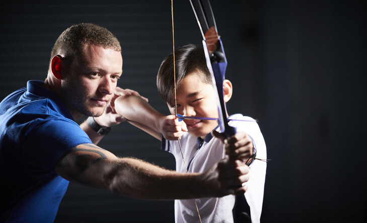 instructor helping boy aim bow and arrow