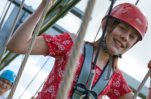 smiling girl holding ropes on aerial trekking course