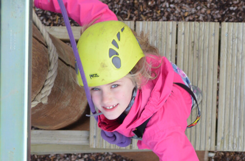 Girl in pink jacket and yellow helmet on high ropes course