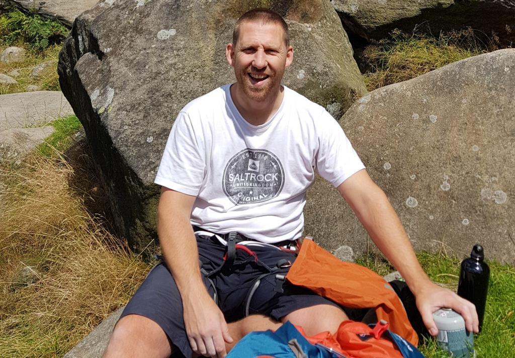 smiling man sat by rocks with climbing equipment